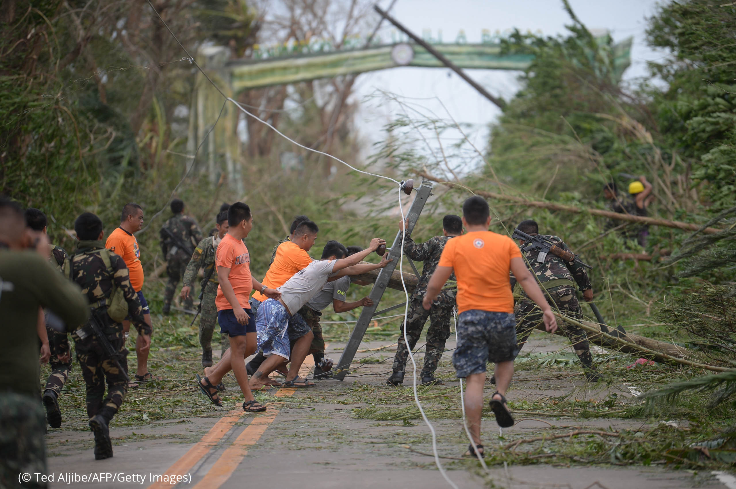 Men clearing road of debris and toppled electric posts (© Ted Aljibe/AFP/Getty Images)