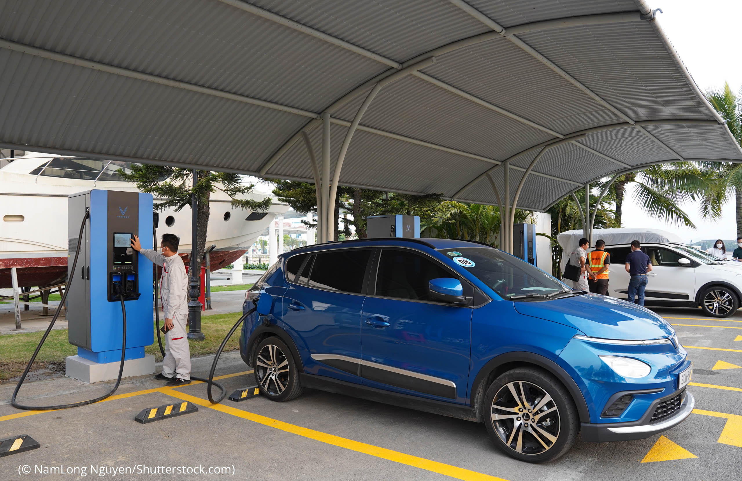 Electric vehicles charging at charging station with people beside them (© NamLong Nguyen/Shutterstock.com)