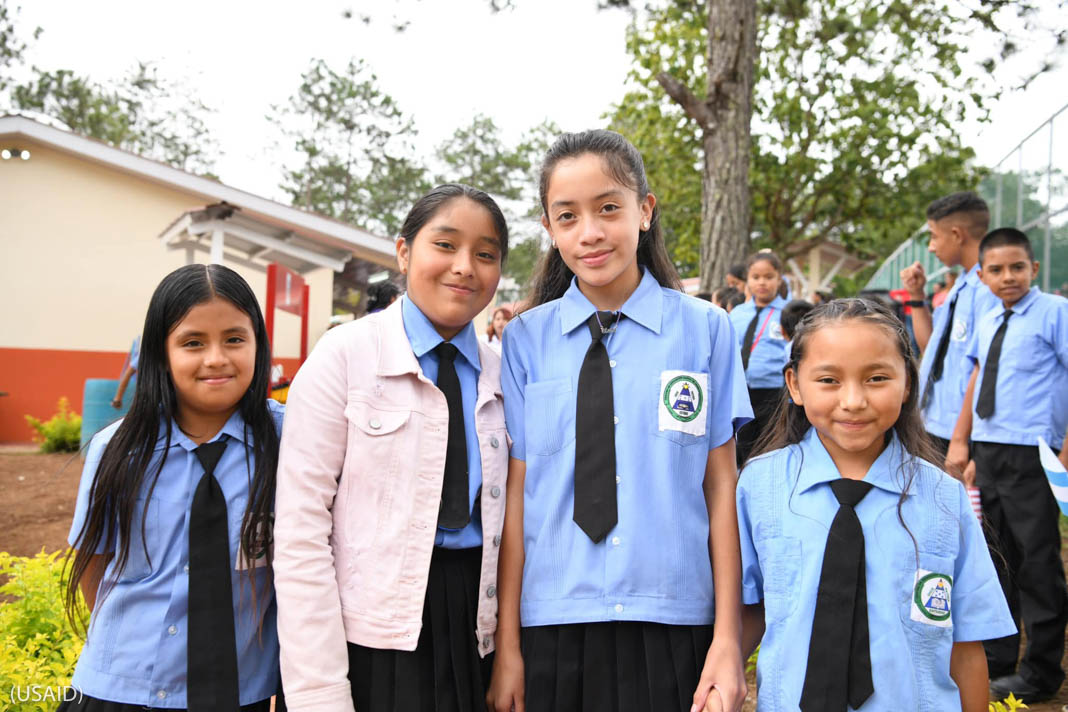 Students in uniform, with four smiling girls posing in foreground (USAID)