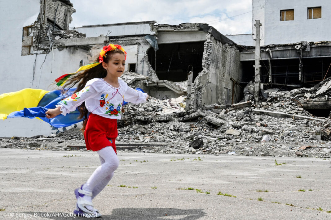 Girl with Ukrainian flag running past rubble (© Sergey Bobok/AFP/Getty Images)