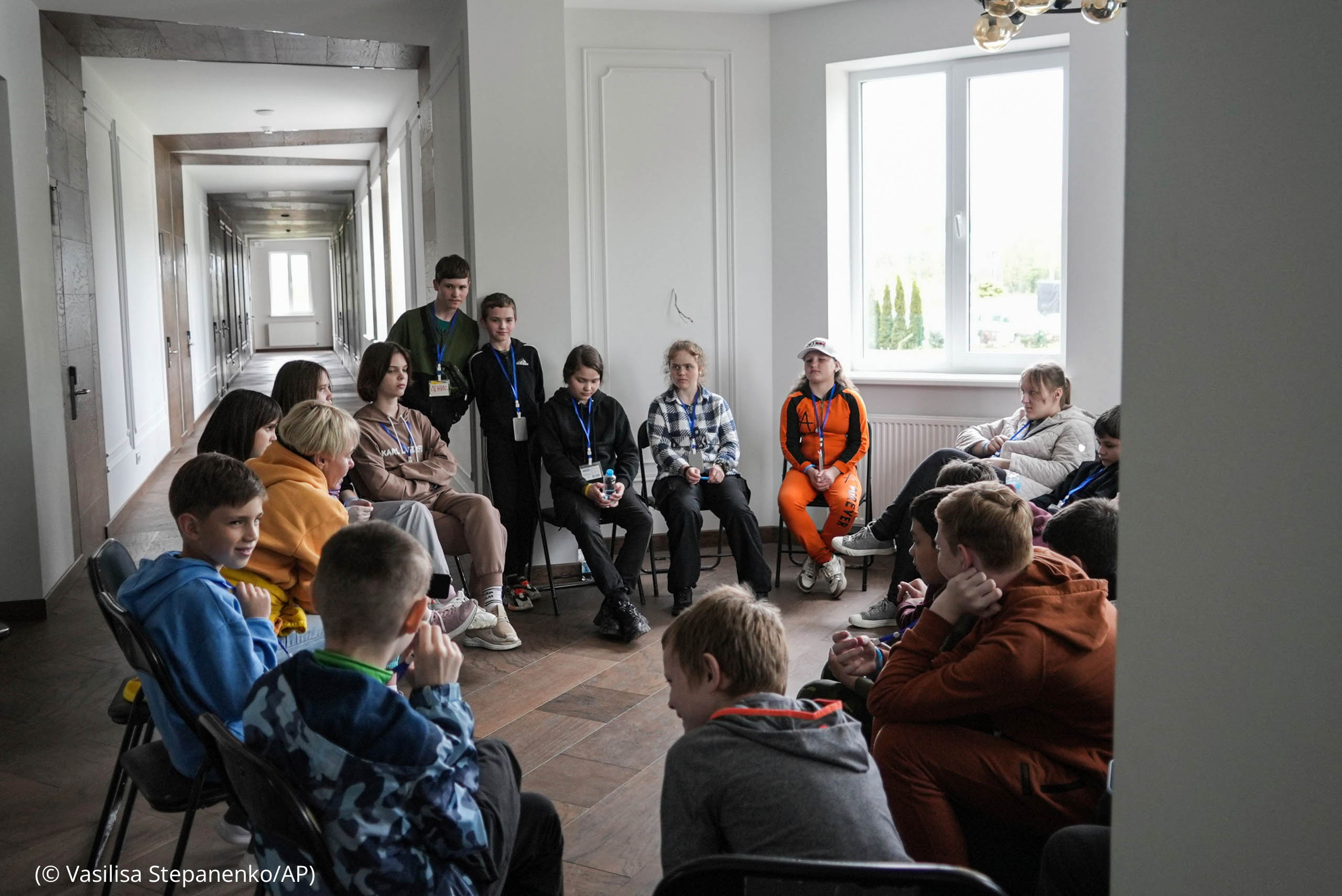 Circle of children sitting in chairs listening to person speak (© Vasilisa Stepanenko/AP)